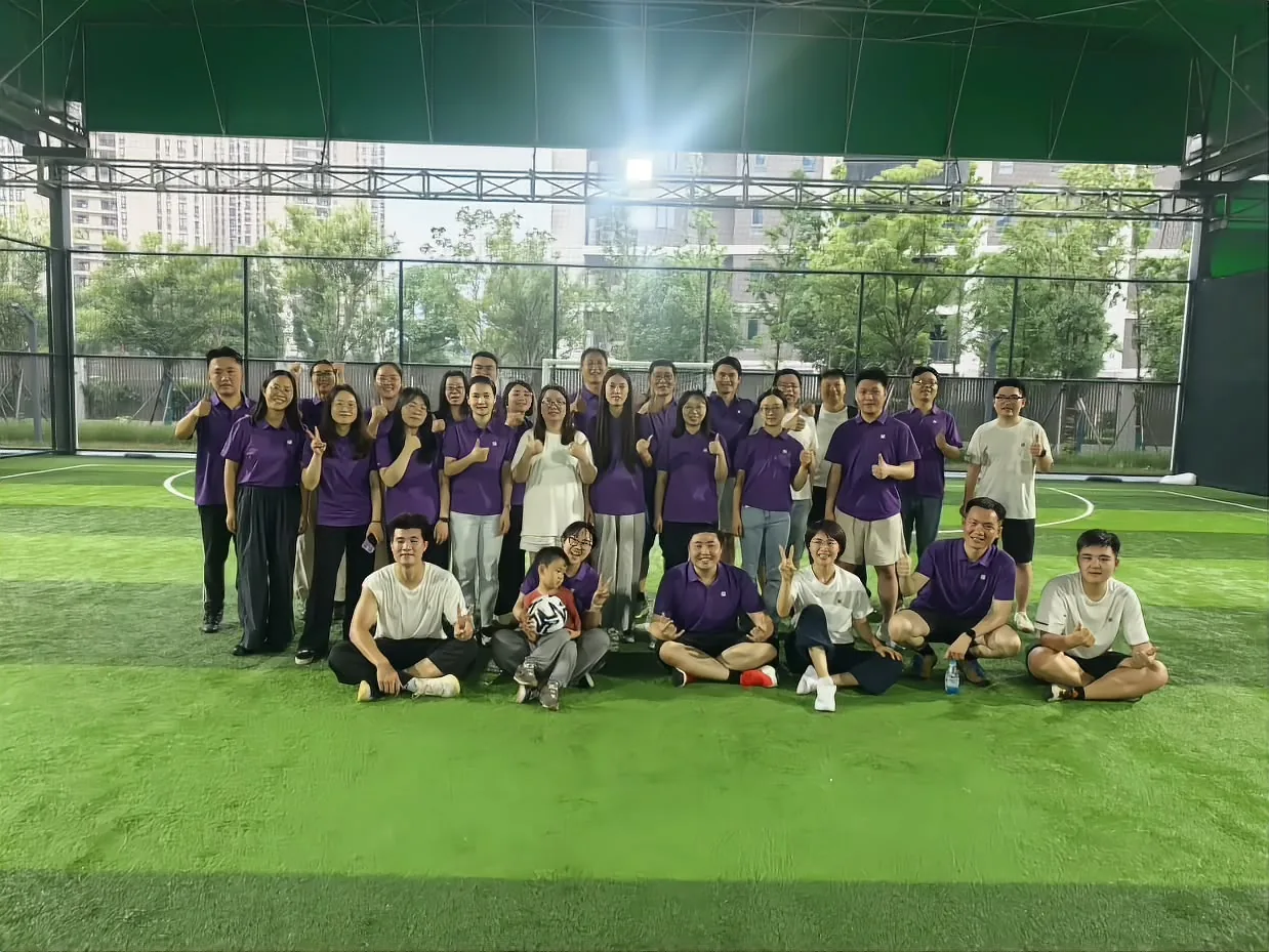 Colleagues posing at the side of the pitch, most in the brand purple kit; a child sits up front holding a football