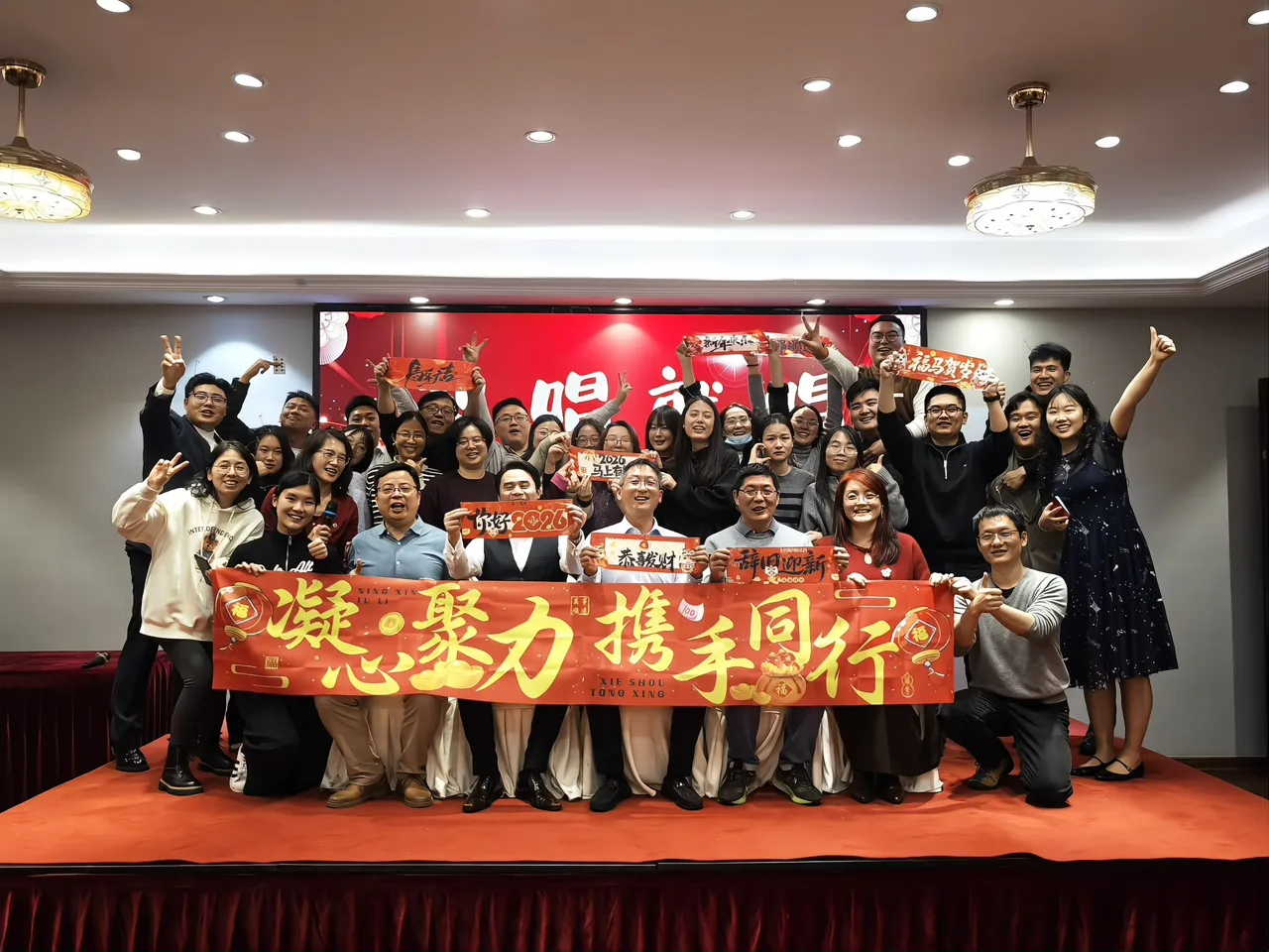 Colleagues at the New Year gala holding a banner reading “United in Purpose, Moving Forward Together”, with red celebratory placards in their hands