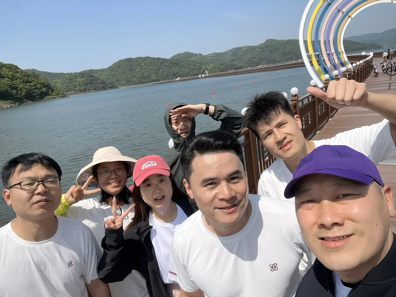 Colleagues on a lakeside outing, with the colourful arch, the lake, green hills and cyclists on the boardwalk behind them